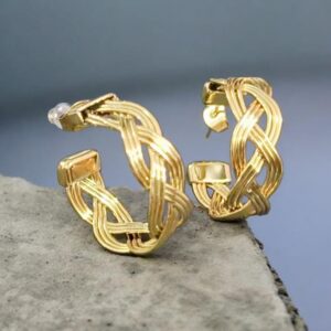 Close-up of Jewel & Choco gold braided hoop earrings with woven wire texture on a grey stone background.